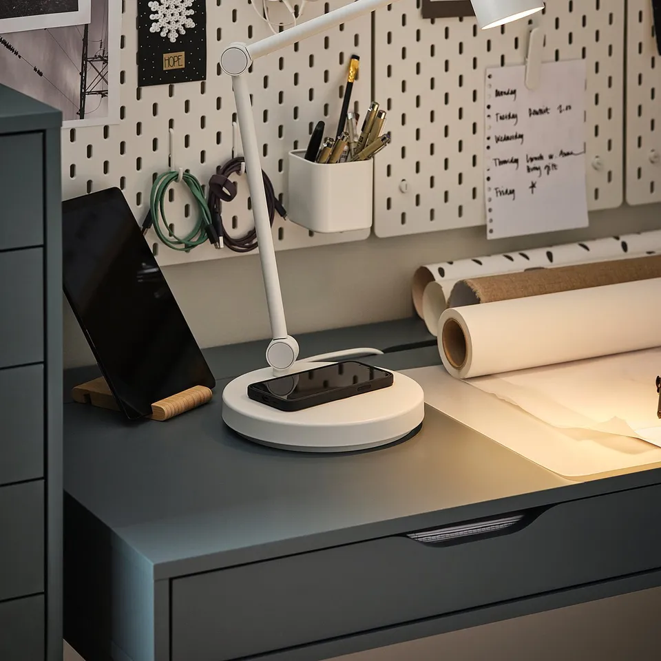 Organised desk with grey NYMÅNE lamp, white headphones, notepads, and pens on a pegboard wall.