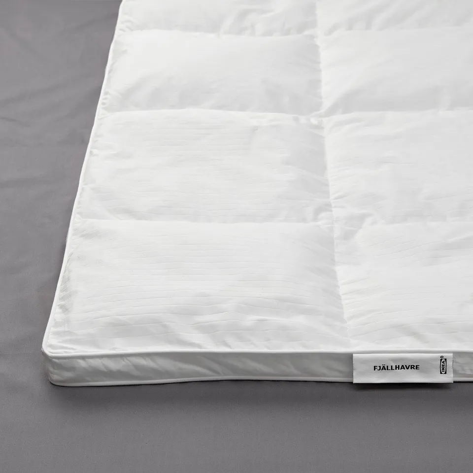 A plush, white fjällräven duvet displayed on a bed, featuring stitched sides for warmth, indicating high-quality comfort and luxurious materials.