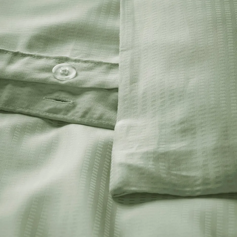 Close-up of LÄKEVÄNDEROT duvet cover with smooth, textured green pattern and functional button.