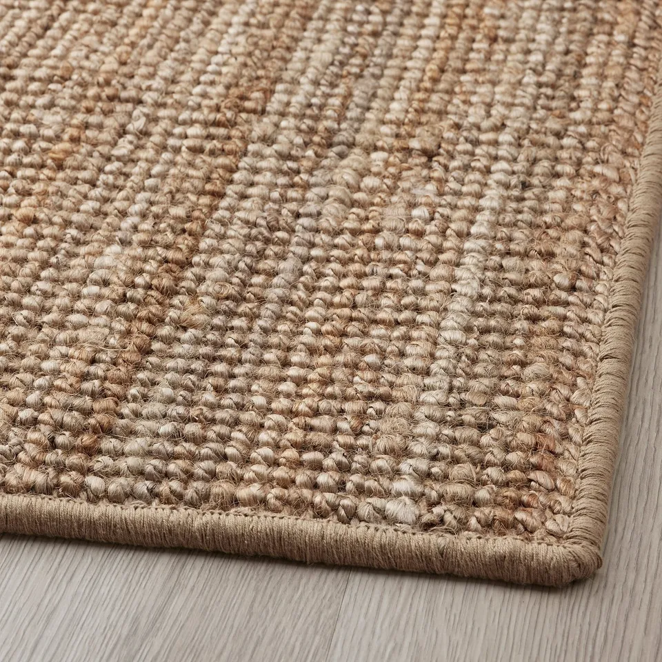 Beige jute rug with intricate weaving, lying flat on wooden floor, showing quality texture and design.