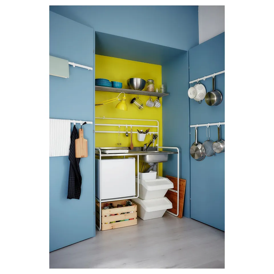 Compact blue and yellow kitchen with stainless steel sink, hanging pots, and vibrant decor.