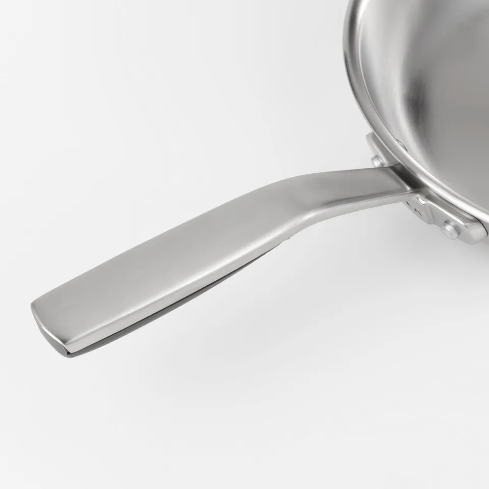 Close-up of SENSUELL frying pan handle. Sleek stainless steel finish, ergonomic design with silicone underside for secure grip.