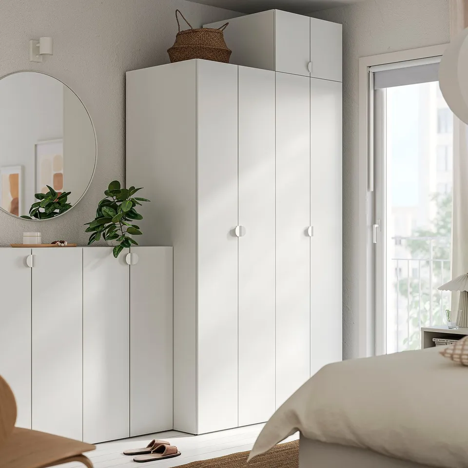 Minimalist bedroom with white LASTARE wardrobe and shelves. Plant, mirror, and shoes nearby.