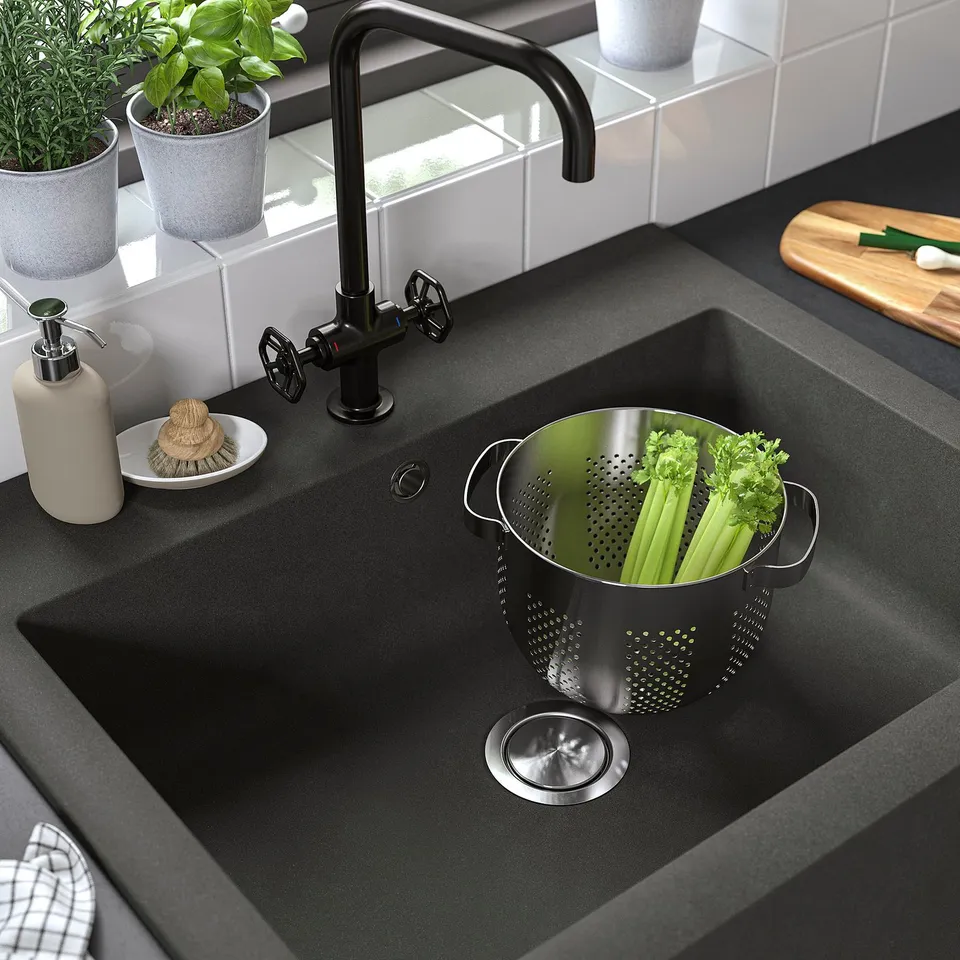 Modern kitchen sink with grey quartz, black tap, vegetables in colander.