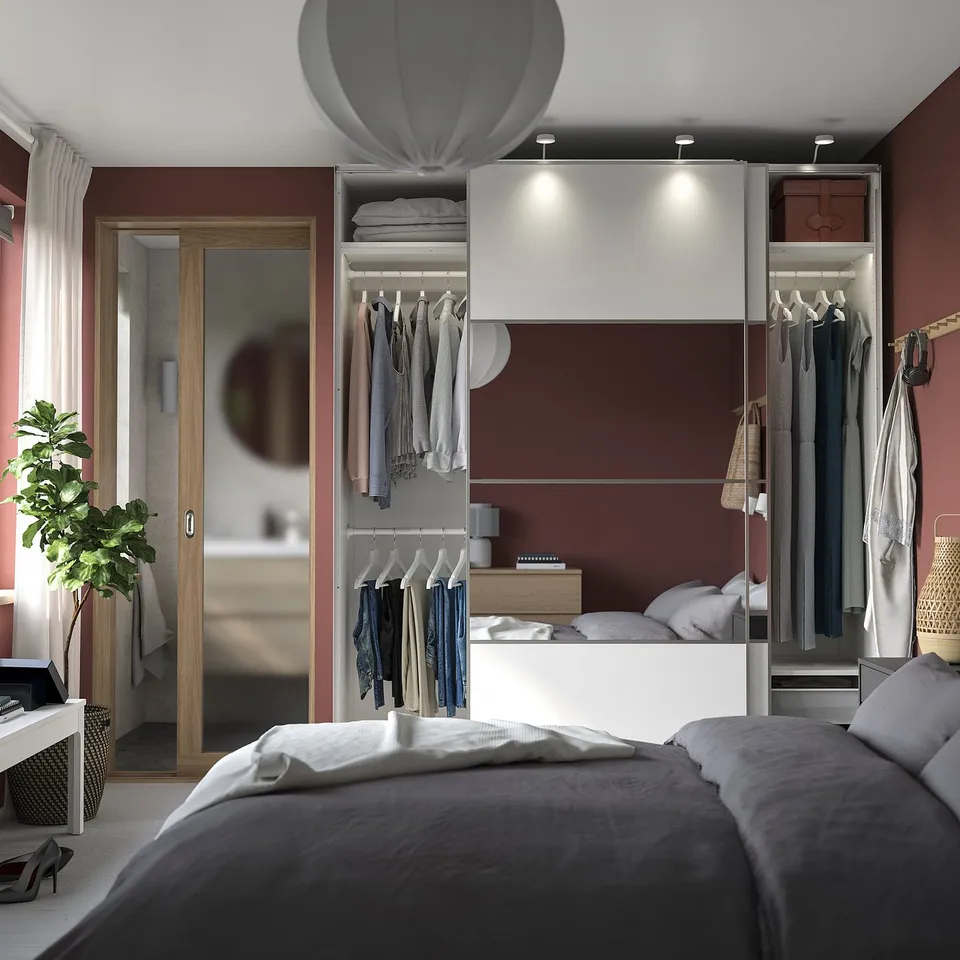 Modern bedroom with PAX wardrobes in white and burgundy, bed with grey bedding, and a plant.