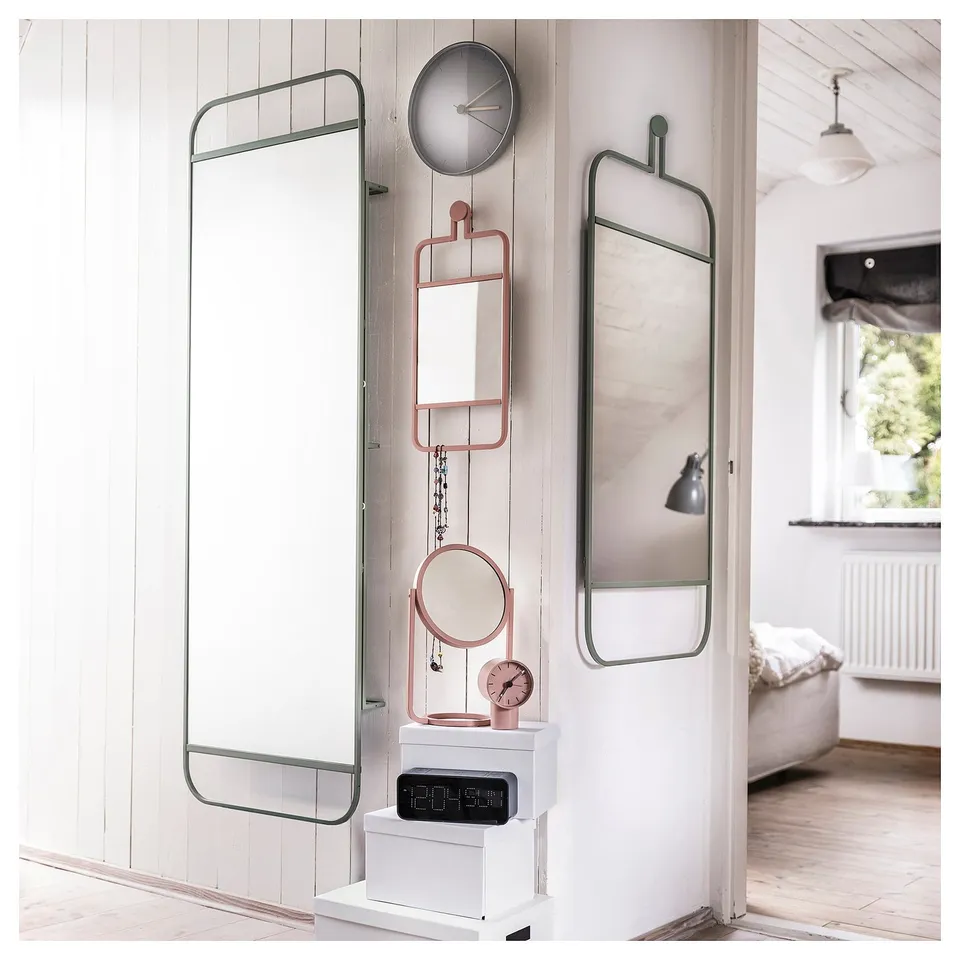 Modern bedroom with GRANVÅG mirror. Silver-framed, it reflects a minimalist nightscape with clock and lamp.