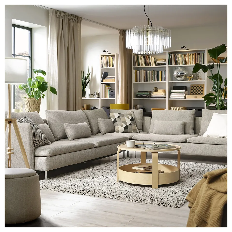 Modern living room with light grey sofa bed, wooden coffee table, chandelier, and bookshelf with books and plants.