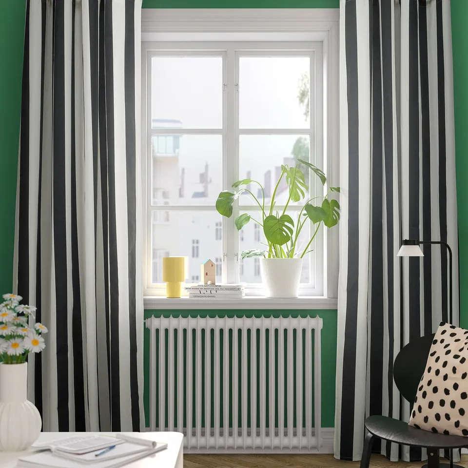 Room with striped curtains, plant, books, desk, lamp, flowers.