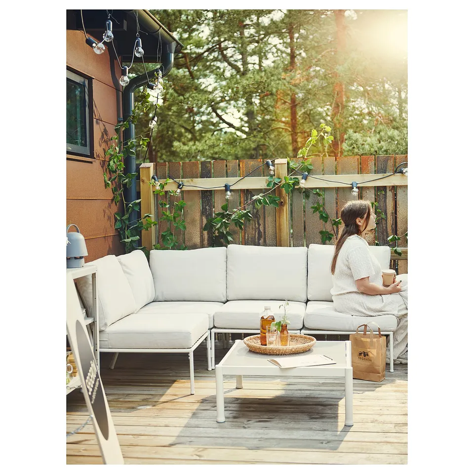 Relaxing person on white outdoor furniture. Modern, clean design with sun-lit trees.