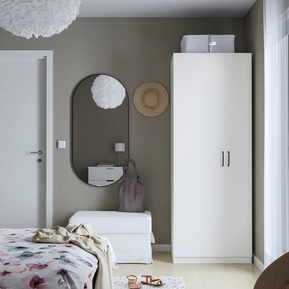 Modern bedroom with white PAX wardrobe, round mirror, and floral bedding against a dark wall.