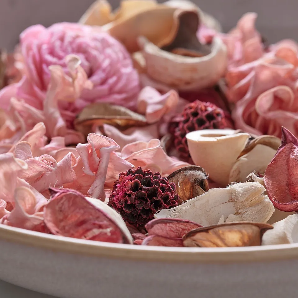 Bowl of colourful, dried flowers & plant parts, pink hues dominate, natural & decorative.