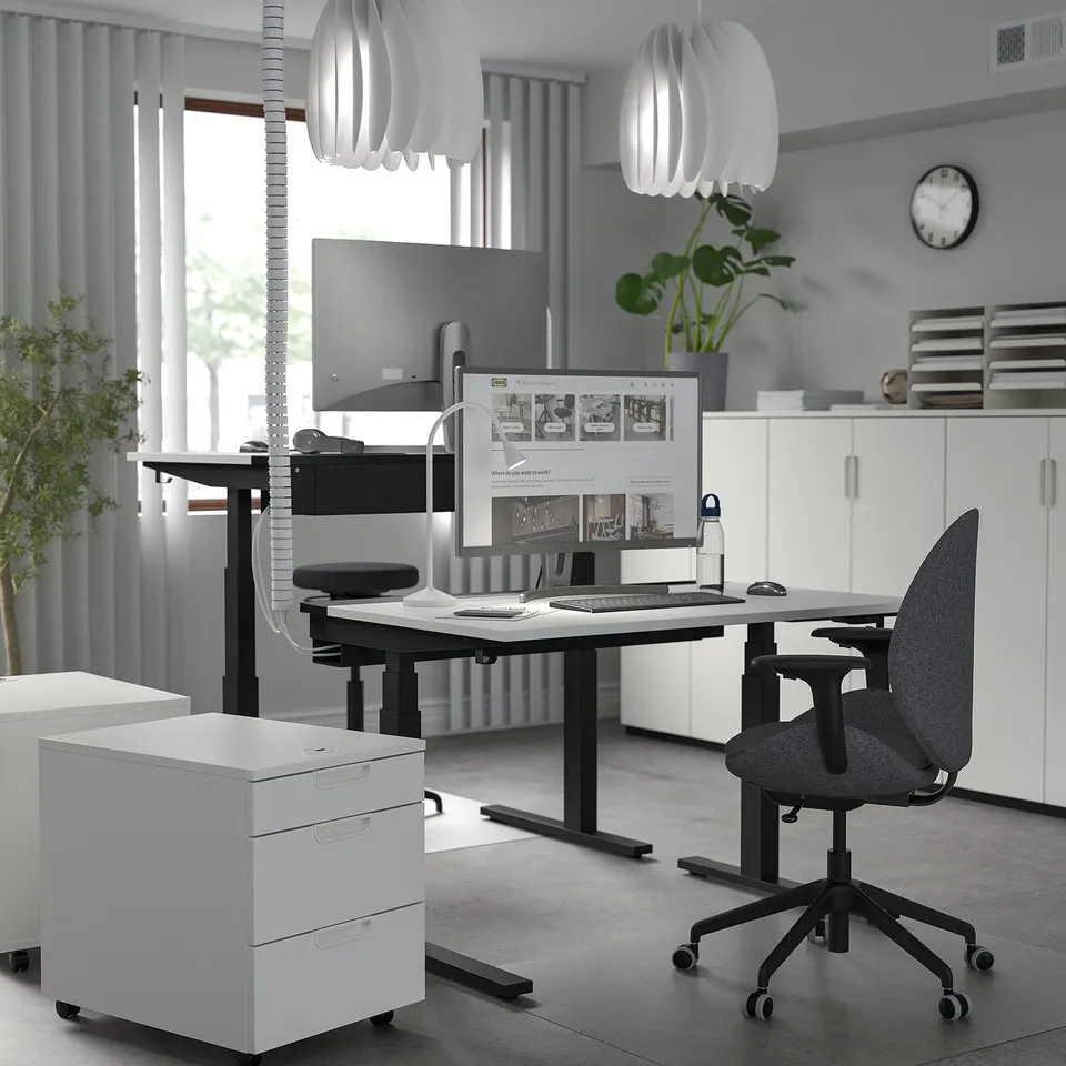 Modern white home office setup. Height-adjustable MITTZON desk, ergonomic chair, and sleek cabinetry. Computer and accessories neatly arranged.