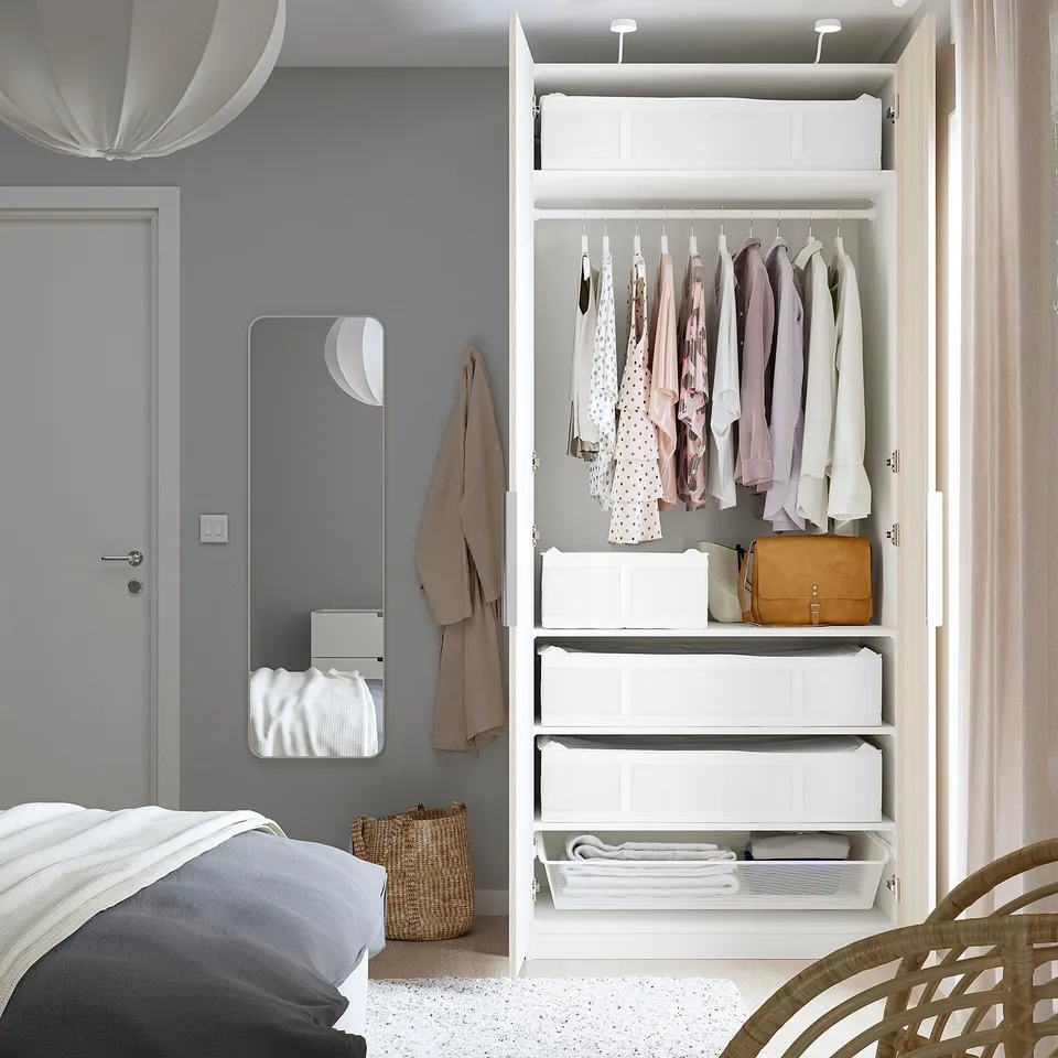 Ordered bedroom with white wardrobe, storage boxes, and large mirror.
