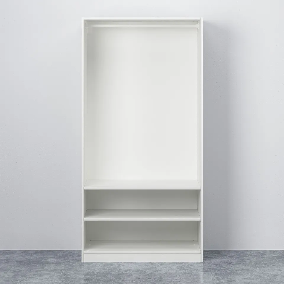 An empty, white, two-shelf PAX storage unit standing against a plain wall. It has adjustable feet and requires wall mounting.