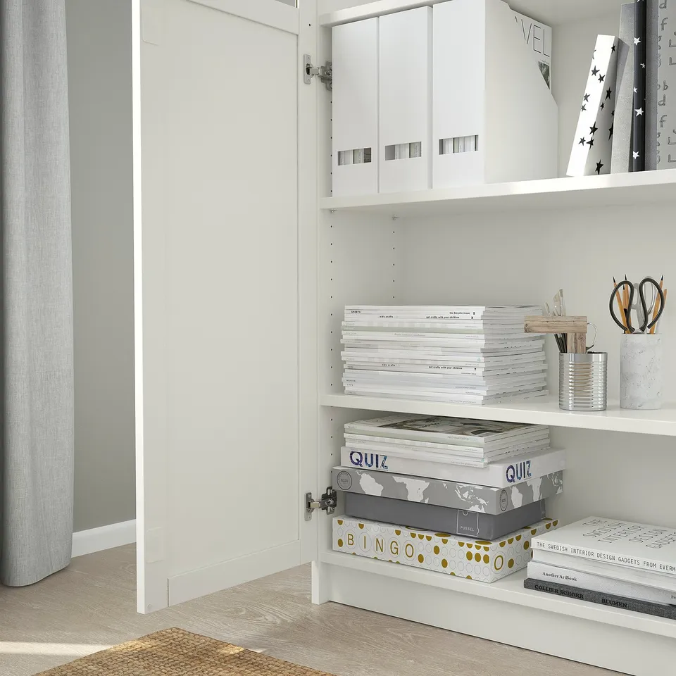 White BILLY bookcase with adjustable shelves, holding white storage boxes, stacked books, and containers with office supplies.