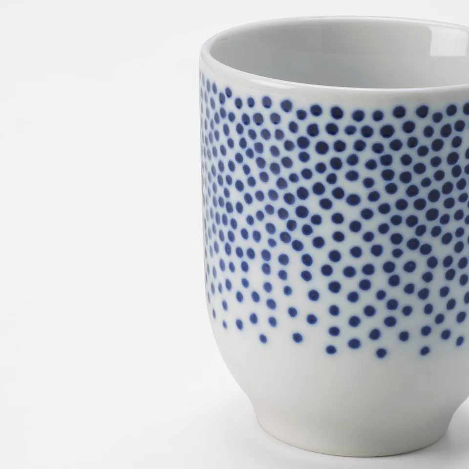 Porcelain mug with intricate blue dots on white background, showcasing detailed craftsmanship.