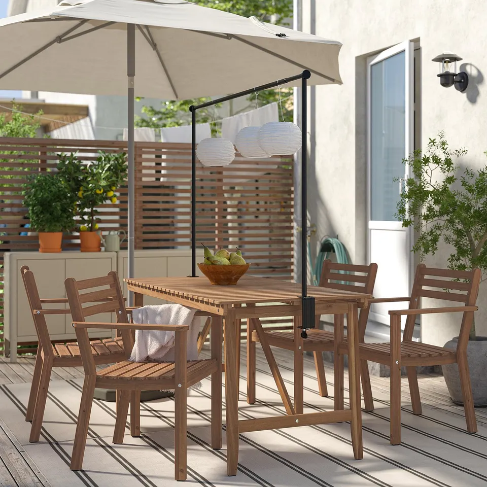 Outdoor setting with ASKHOLMEN brown acacia wood table & four chairs, beige umbrella, lanterns, bowl of fruit. Cosy, stylish patio.
