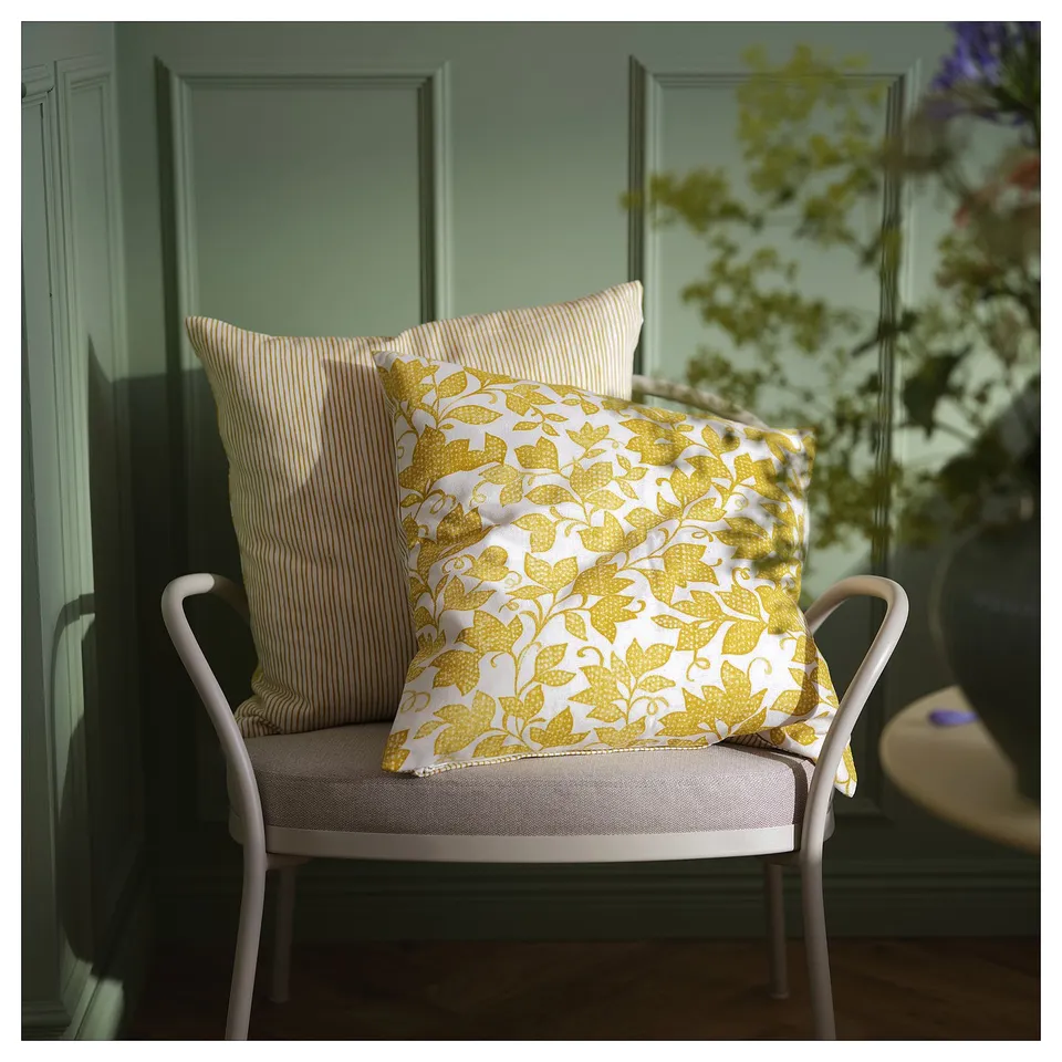 Bright yellow throw pillows on a white chair against a green wall. One pillow has a leaf pattern, the other has stripes.