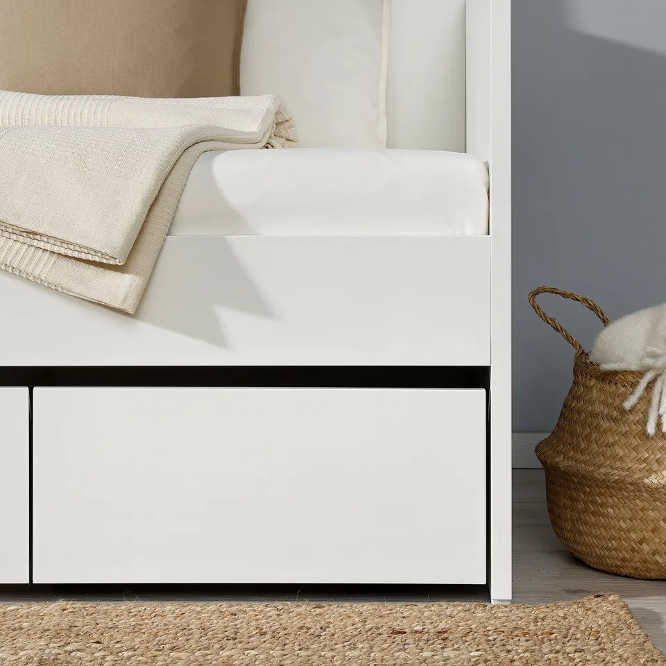 A modern white daybed with storage. Folded blanket and woven basket on the side.
