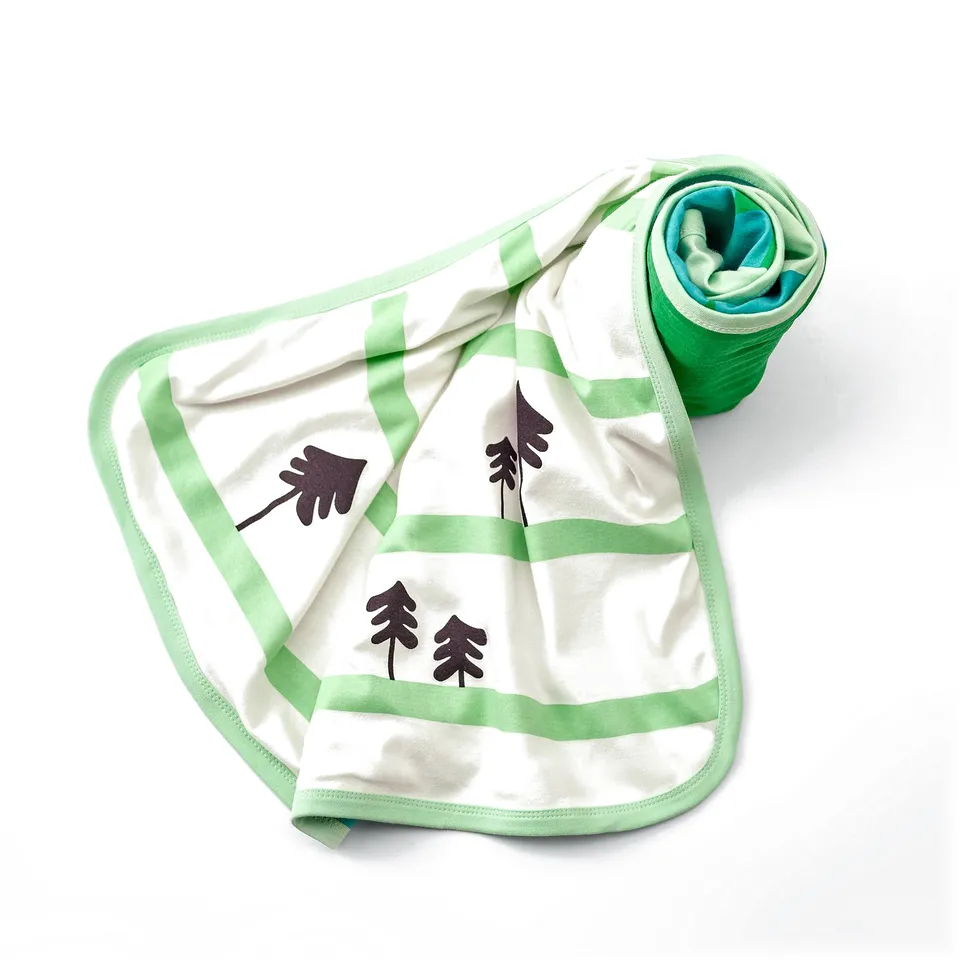 Green and white cotton baby blanket with tree patterns, edges rolled up for display.