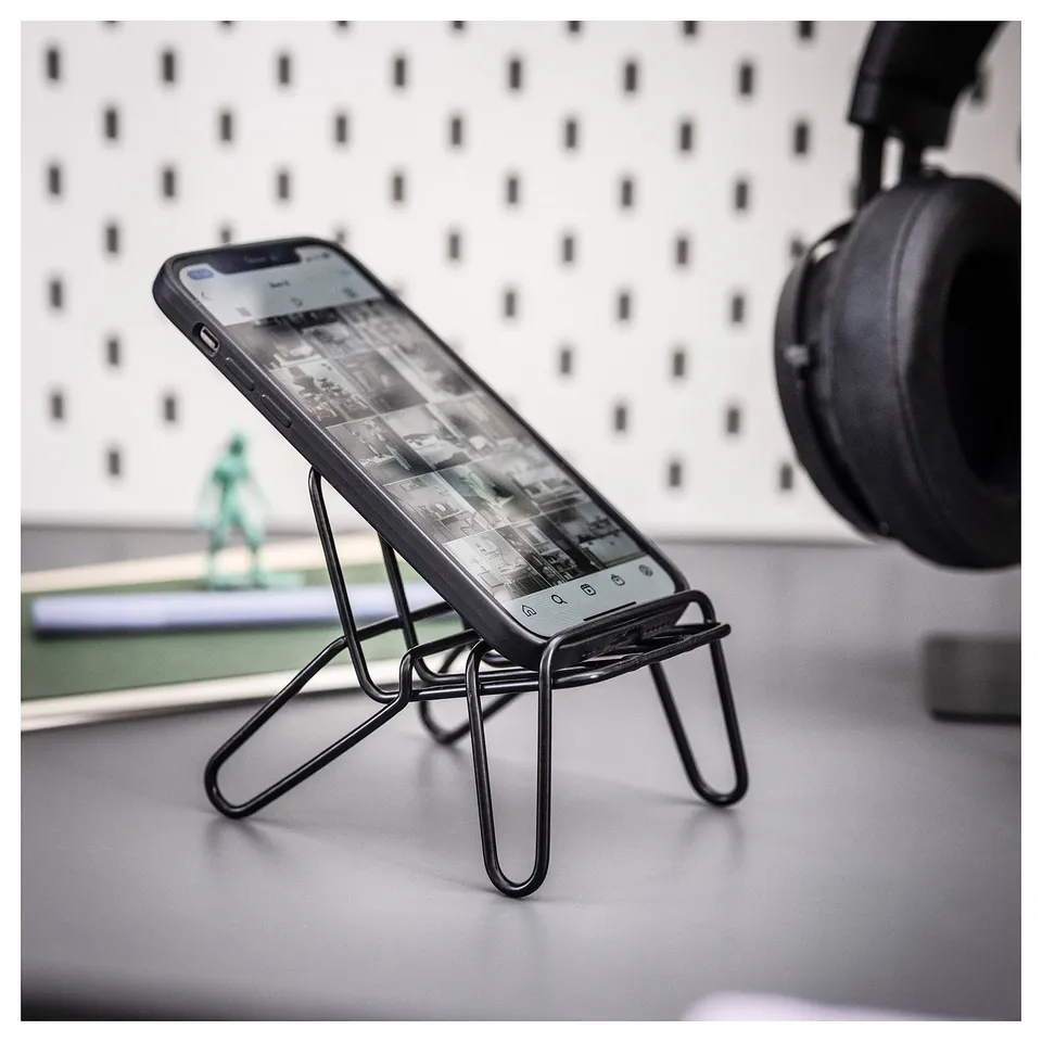 A mobile phone holder named KRUBBET, which is black and made of steel. It supports a phone in various positions while charging.