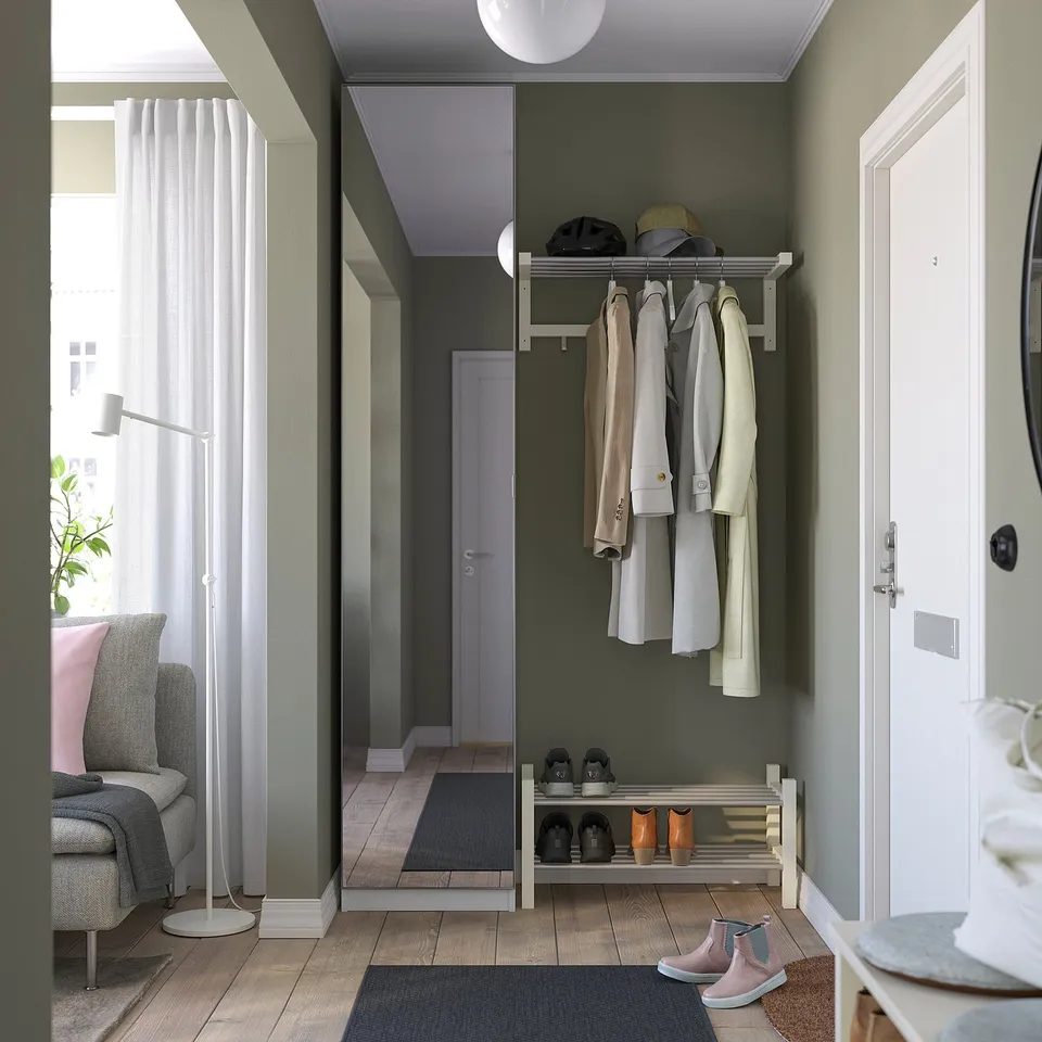 Modern entryway with coats on green PAX wardrobe, hats, shoe rack, and rug.