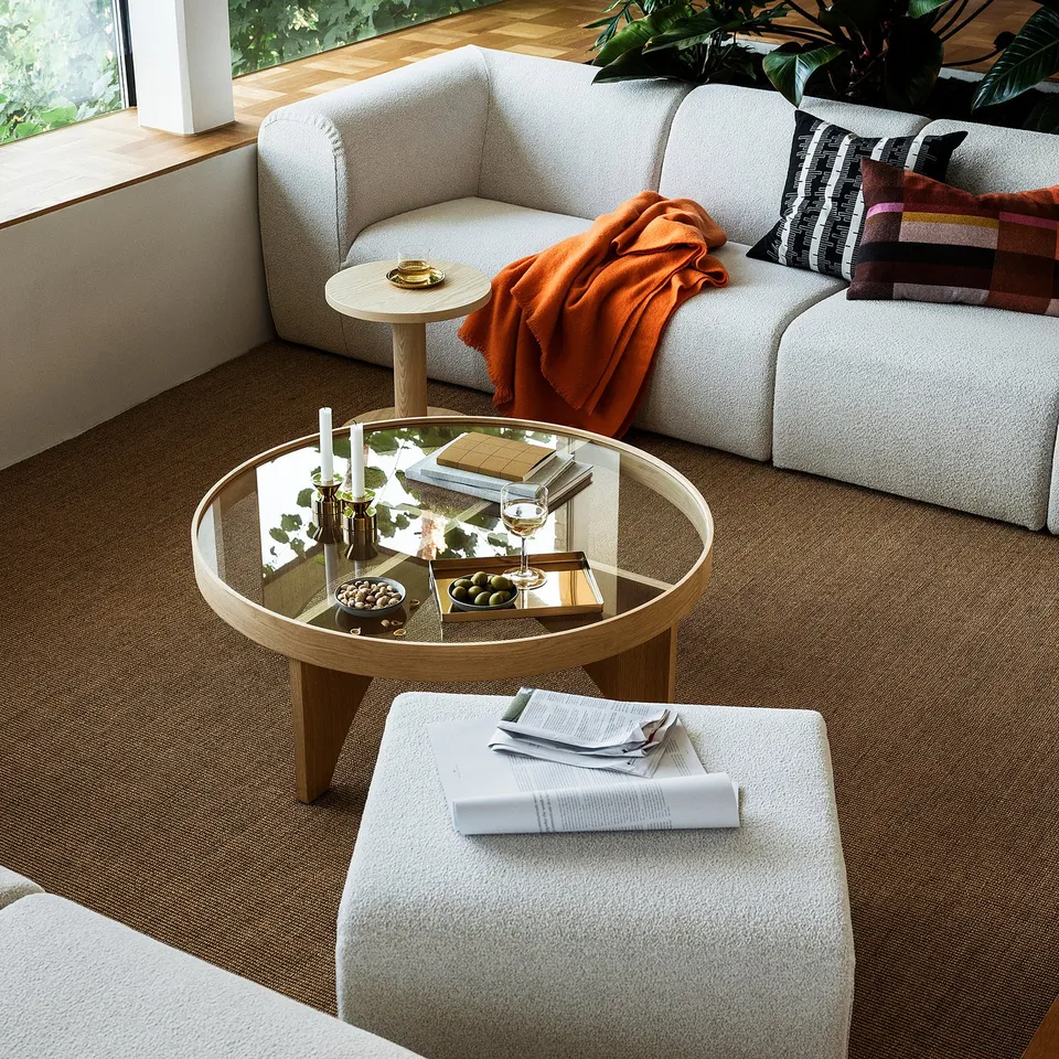 Modern living room with glass coffee table, white l-sofa, colourful pillows, and scandinavian design.
