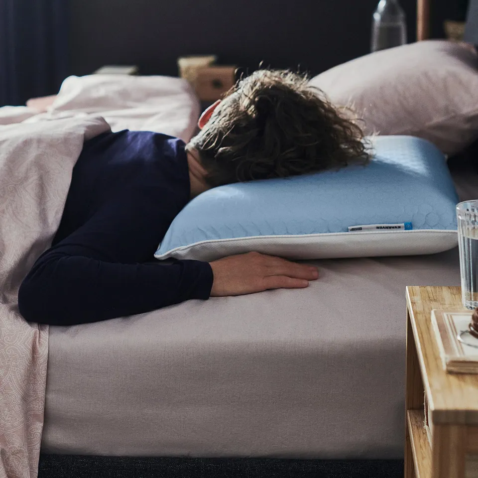Person sleeping on bed with blue KVARNVEN pillow.