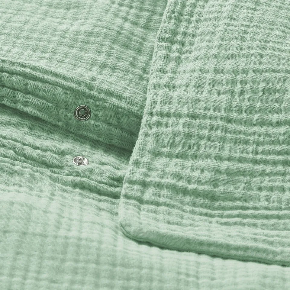 A green gots-certified organic cotton duvet cover with metal press-stud closure at the bottom. Wavy, airy texture and envelope pillowcase closure.