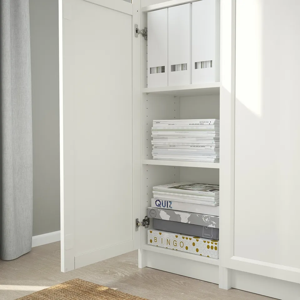 White BILLY bookcase with adjustable shelves storing books and games, neatly organised.