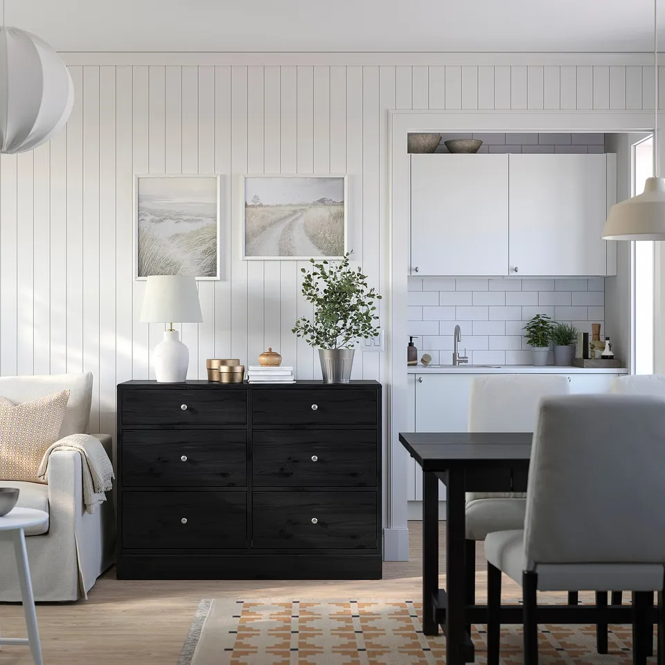 Modern living room with black HAVSTA chest, decorative items, grey & white furniture, colourful rug, and kitchen in background.