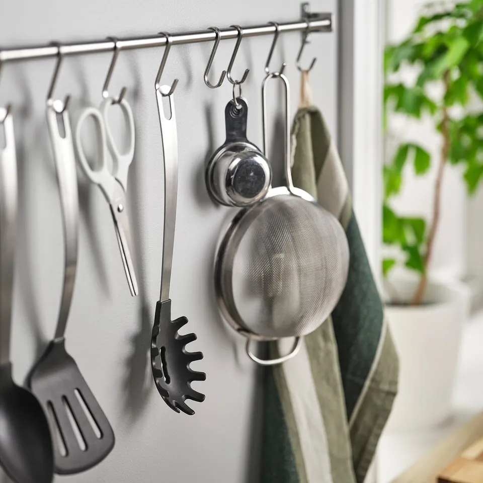 Kitchen tools hang on hooks; includes pasta server, spatula, strainer, and scissors.