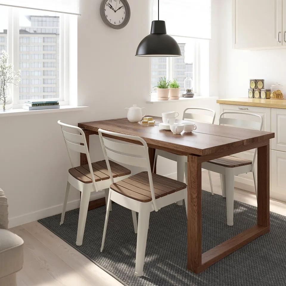 Small dining set with wooden table and white chairs, positioned near a kitchen window with a city view.