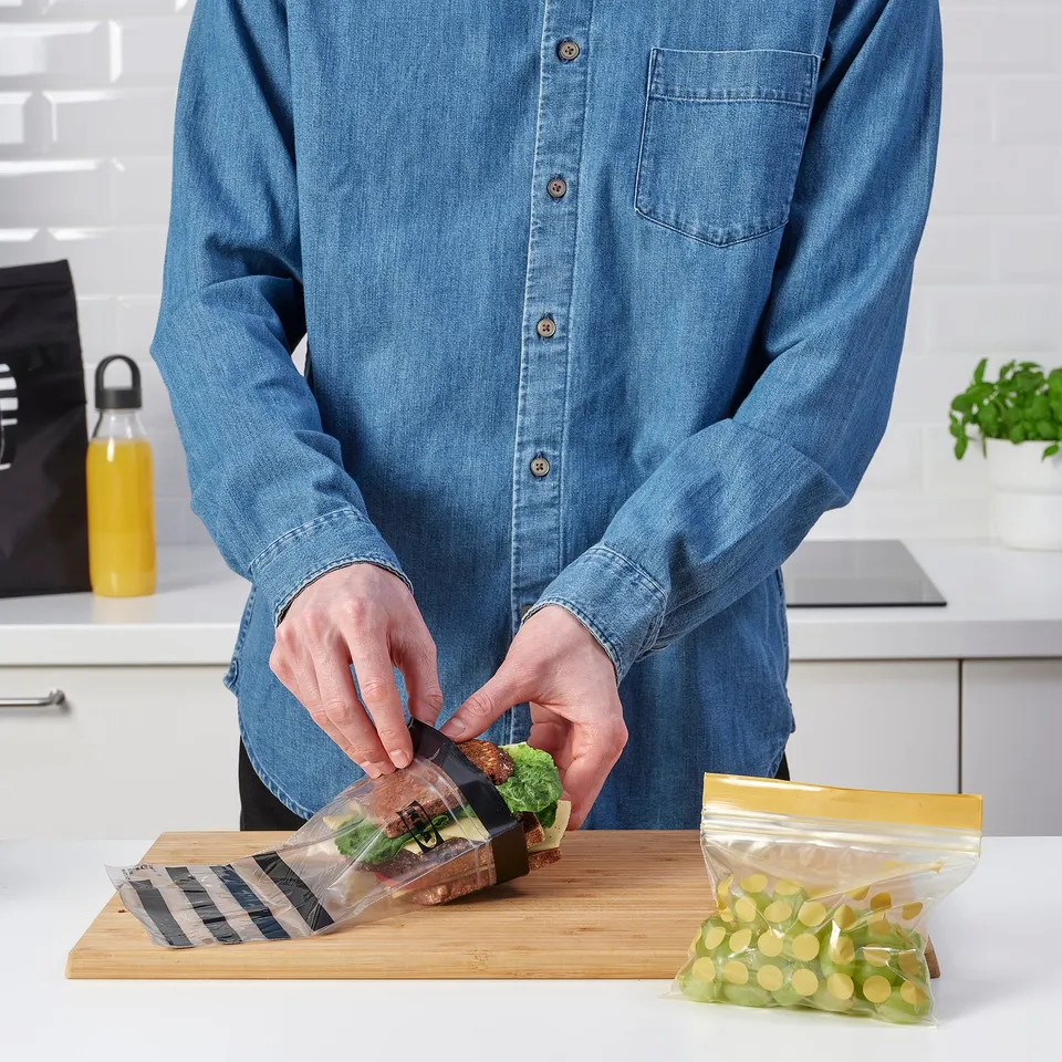 Packing sandwich in reusable ISTAD bag on cutting board, grapes nearby.