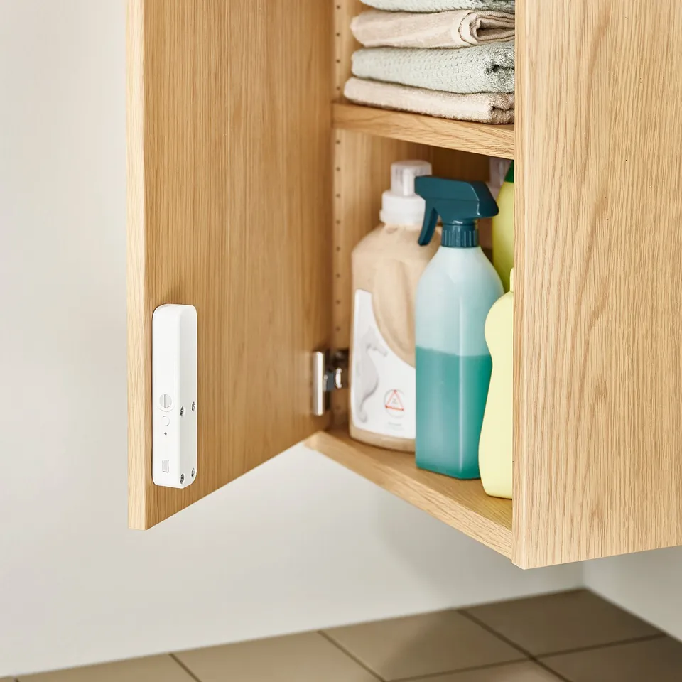Open wooden cabinet displaying cleaning supplies: bottles, sprayer. White nfc-enabled lock, SOLSTOL, mounted on door.