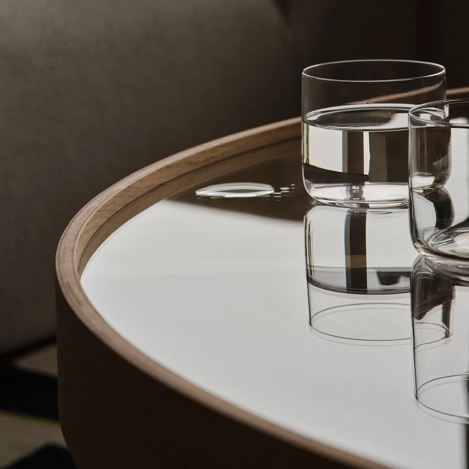 Modern glass table with wooden frame, reflecting light, showcasing elegant design.