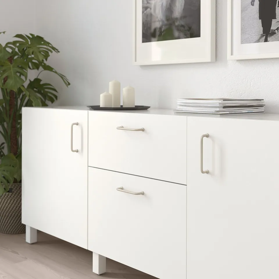 White bagganas cabinet with metal handles, large, holding candles and books.