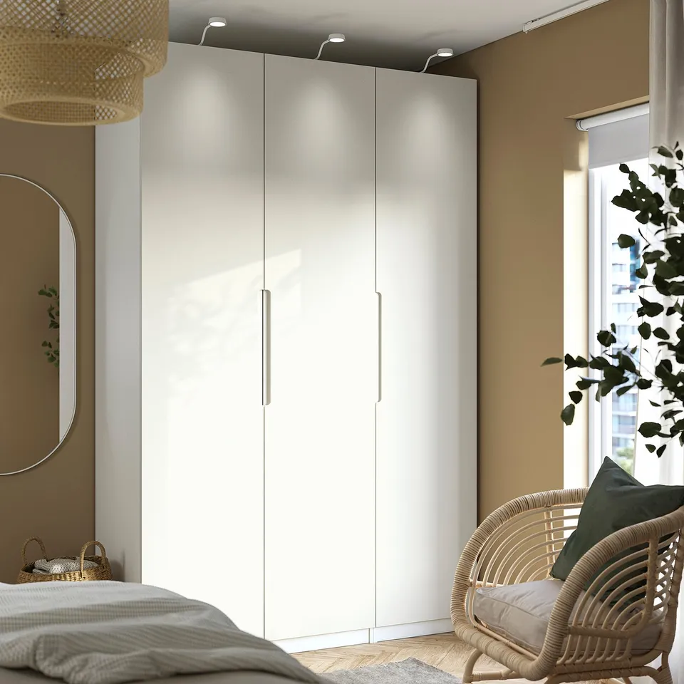 Modern bedroom with white wardrobe, integrated lighting, wicker chair, and plant. Cosy atmosphere.