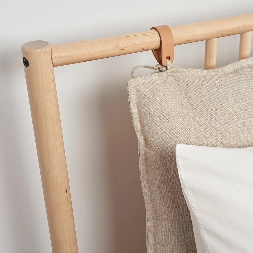 Modern wooden bed frame with leather detail and beige pillow.