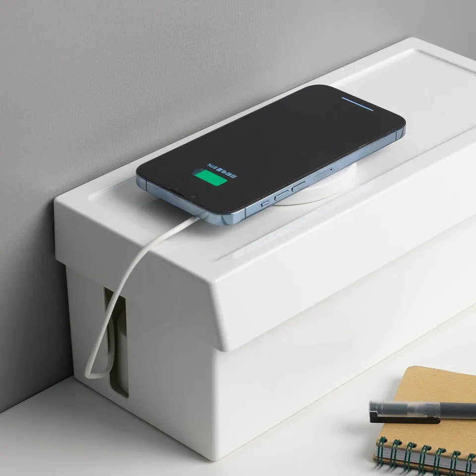 Boxed wireless charger on desk. Smartphone charging, notepad nearby.