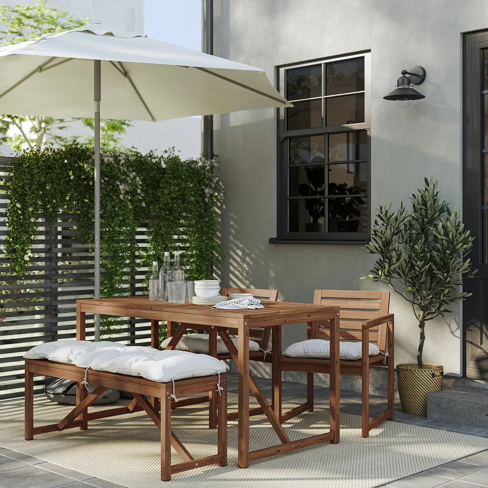 Modern outdoor dining set with wooden table, chairs, and cushions under a large white umbrella.