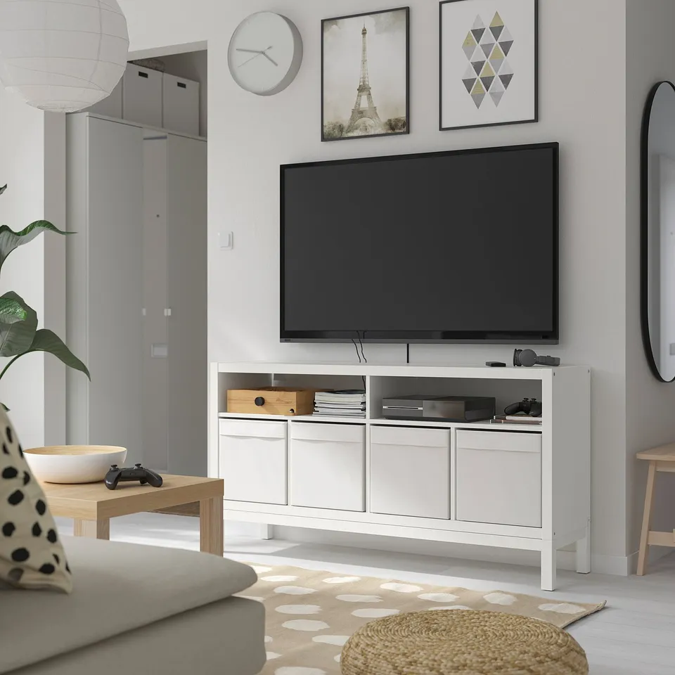 Modern living room with KALLAX tv bench, grey sofa, side table, and rug. Tv and decor on bench, wall art, and stylish lamp.