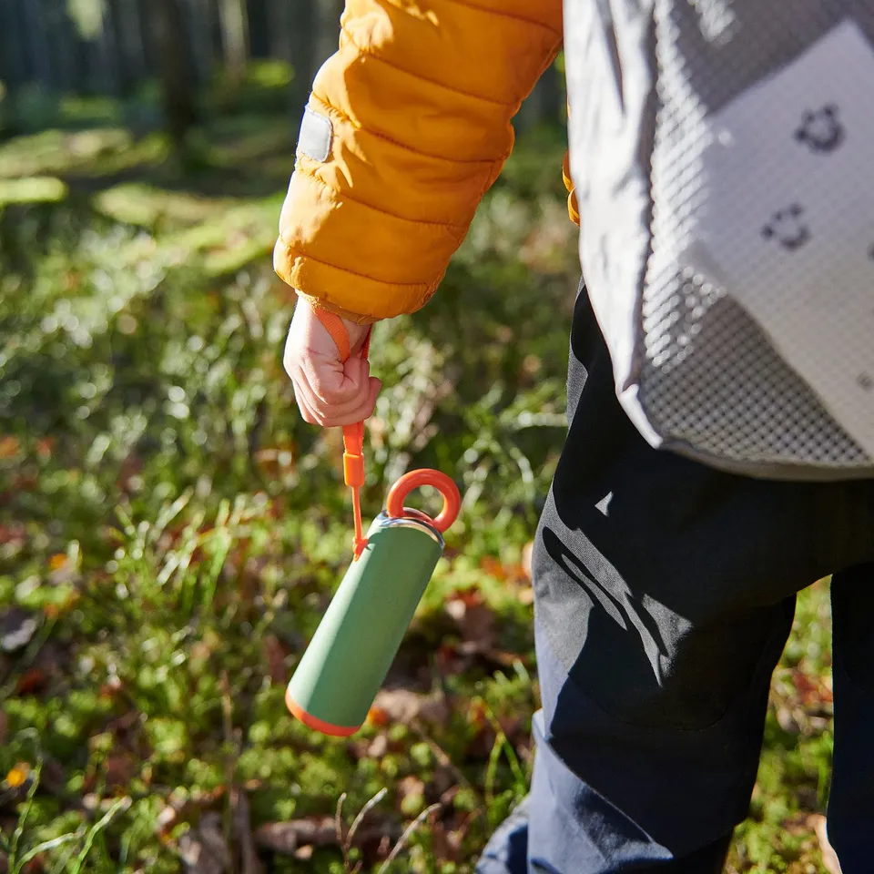 Person holds green led torch, pulling orange string, outdoors.