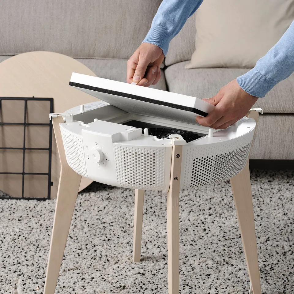 Person instals a philtre into a white STARKVIND air purifier, which removes gases and particles.