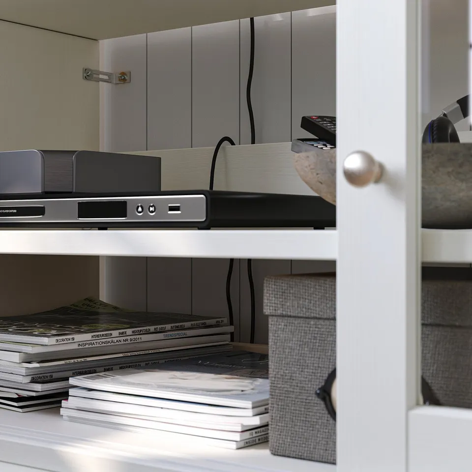 White wooden tv unit with electronics, magazines, and remotes.