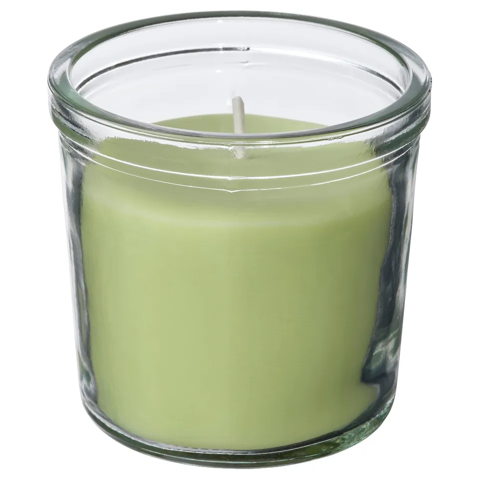 A green LÖVSKOGSLUND scented candle in a clear glass jar, made of plant-based and paraffin wax, with a cotton wick.