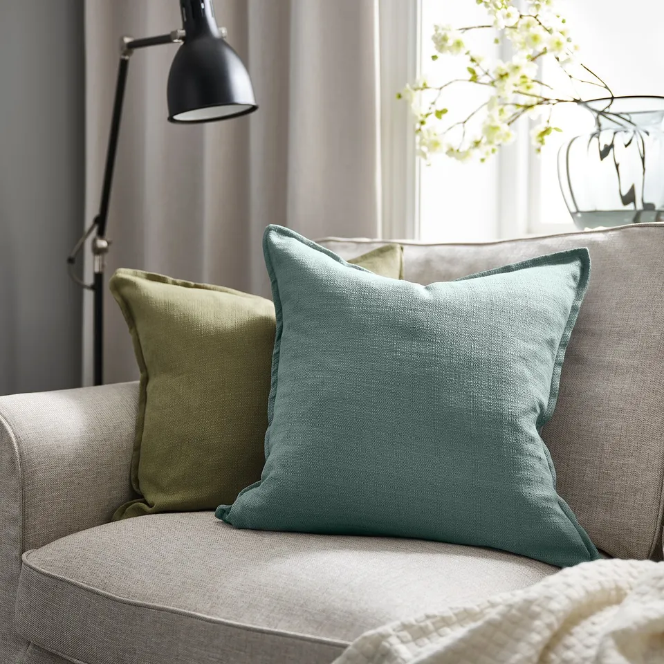 Blue-grey cushion on beige couch, smaller with black lamp and white flowers.