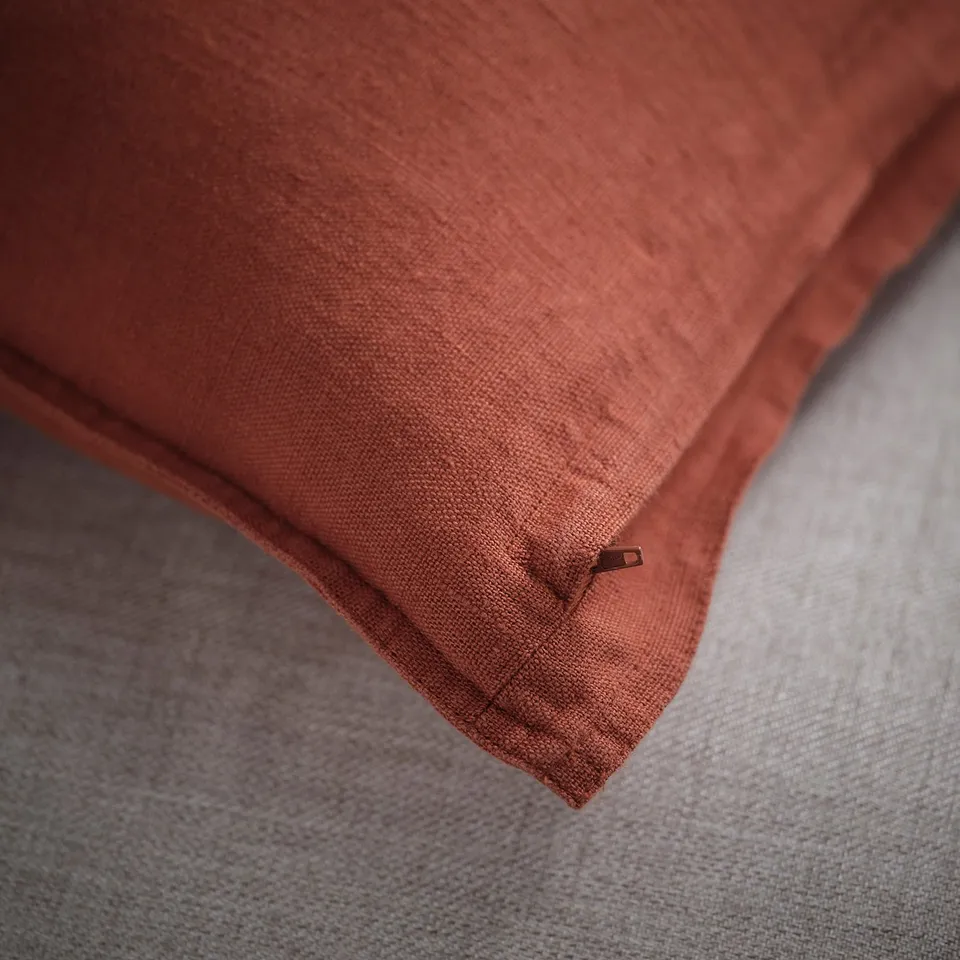 Close-up of a red-brown, textured linen cushion cover with a hidden zip, showcasing its soft and casual look.