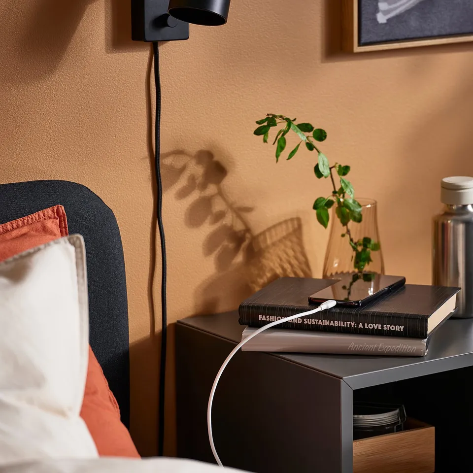 Bedside table with SITTBRUNN usb-c cable, phone, plant, and lamp.