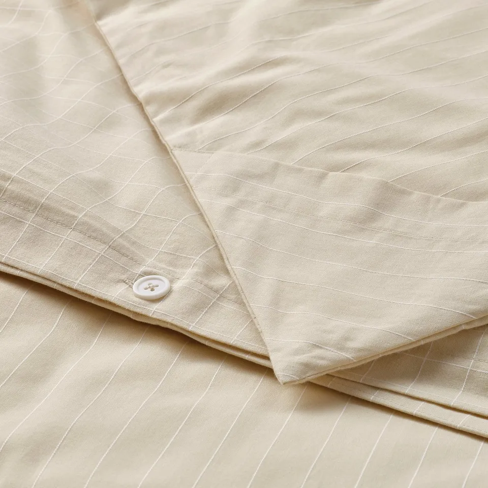 Folded beige duvet cover with check pattern and stripe sides, featuring a button for fastening, designed for easy use and durability.